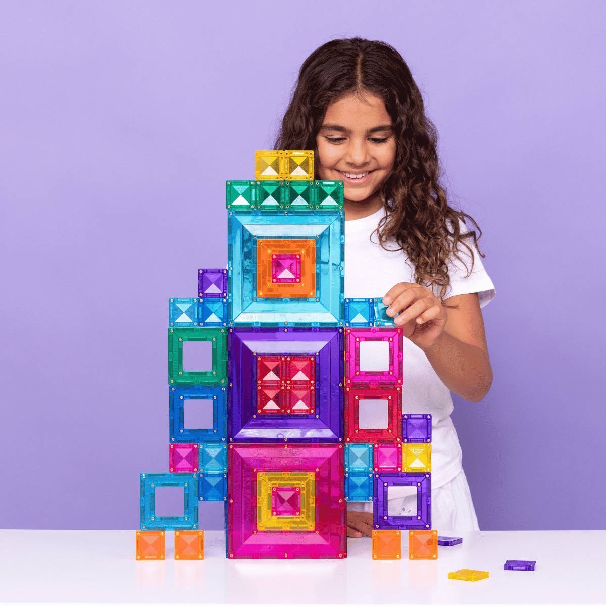 Child playing with colorful magnetic building tiles against a purple background