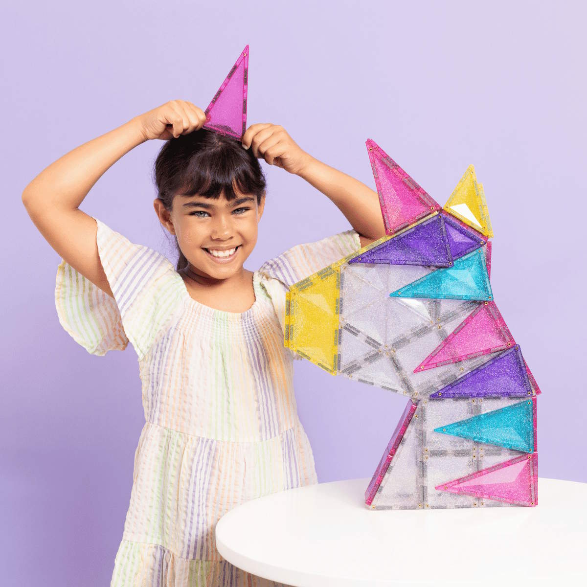Child playing with Connetix Tiles Glitter Unicorn Pack against a purple background