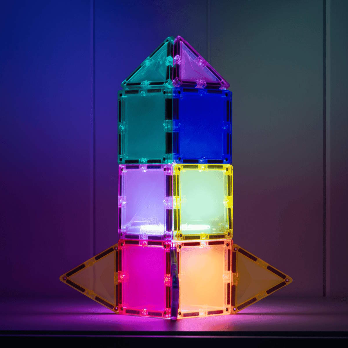 Colorful transparent magnetic tiles tower lit up against a dark background