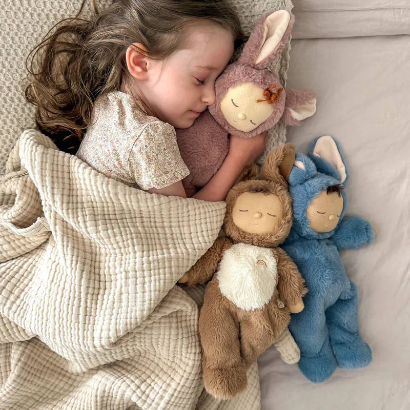 Olli Ella Cozy Dinkum Dolls snuggled in bed with a child. Digby Dog with brown and white fur