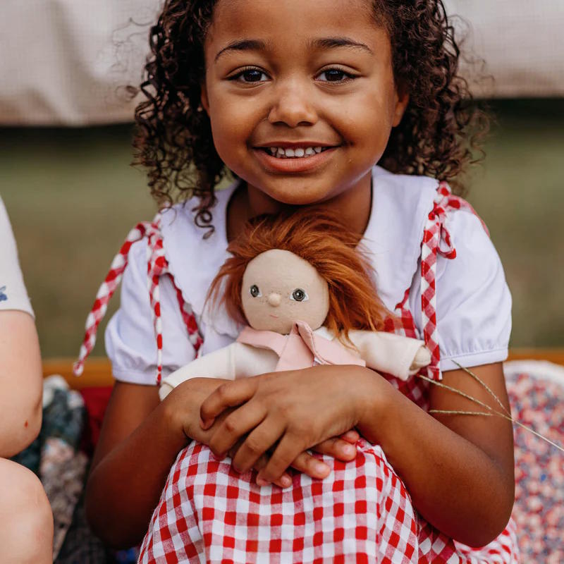 Child holding a redhead doll wearing a red and white checkered dress