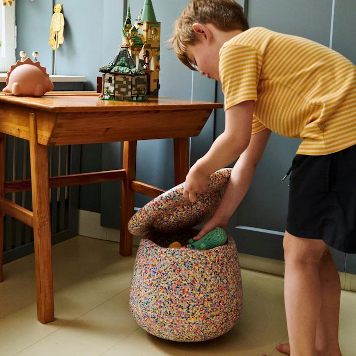 Child playing with toys in a colorful storage basket in a room with a wooden table and decorative items.