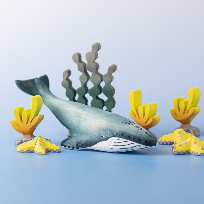 Wooden toy whale surrounded by yellow coral and dark green seaweed
