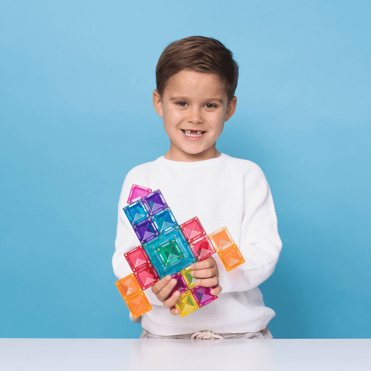 Child holding colorful magnetic building tiles in a spaceship shape against a blue background