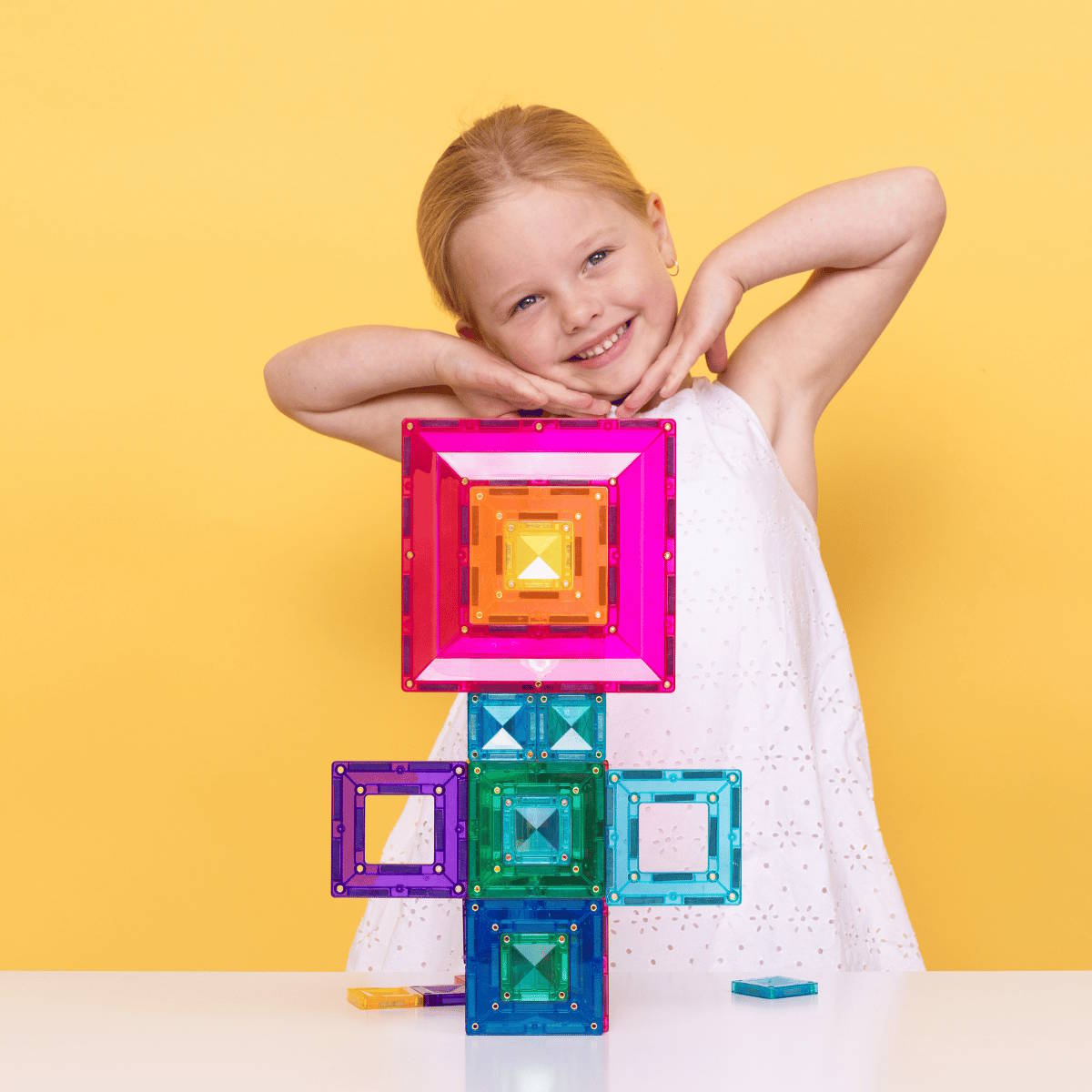 Child posing with colorful magnetic building tiles in a flower shape against a yellow background