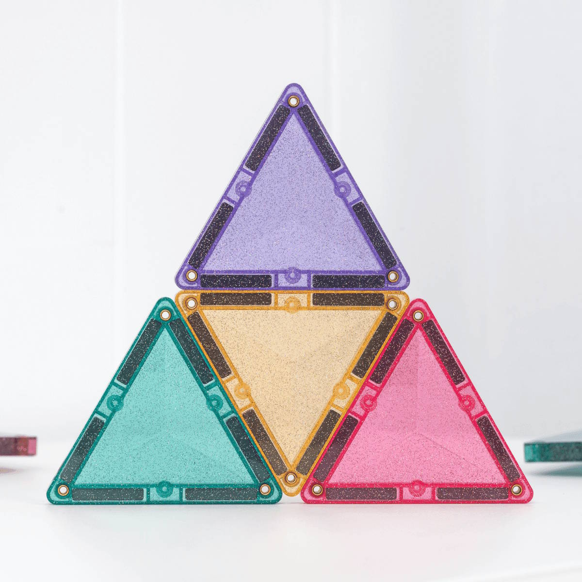 Four triangular colorful Connetix magnetic tiles with glitter on a white background