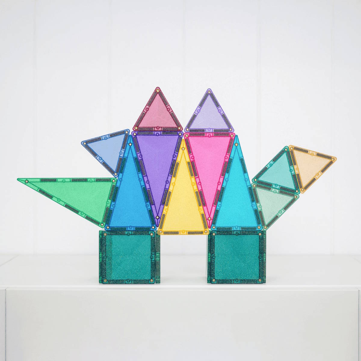 Colorful magnetic triangle building tiles by Connetix in a dinosaur shape on a white background