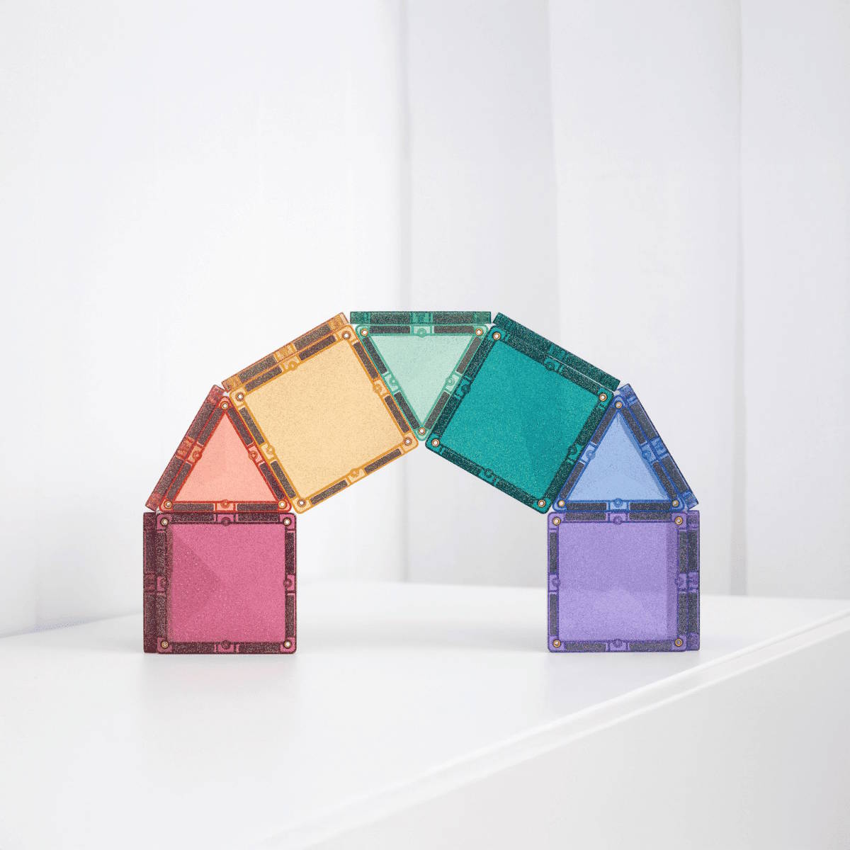 Colorful magnetic building tiles by Connetix arranged in a rainbow arch on a white surface with a white background