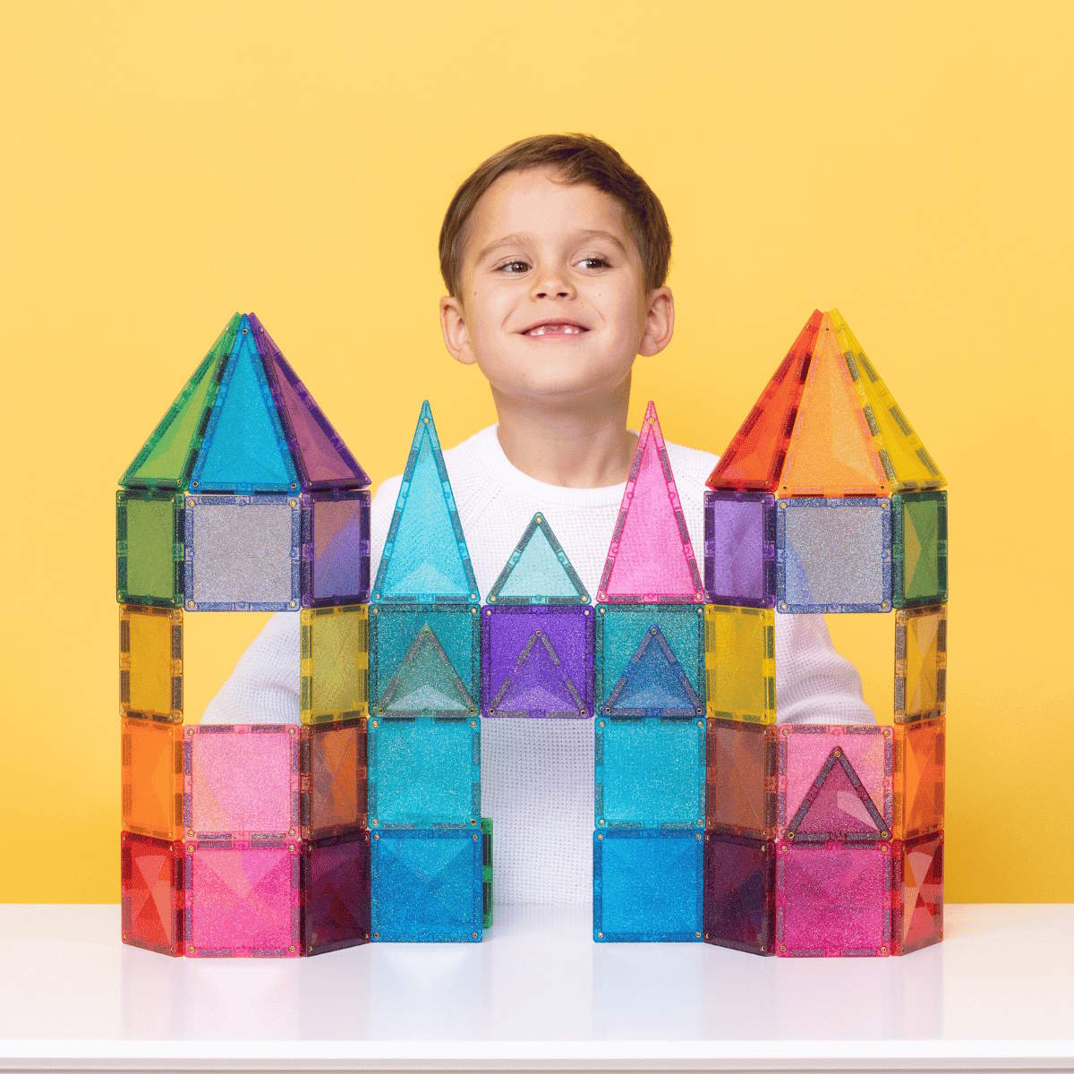 Child with Connetix colorful magnetic building tiles shaped like a castle on a yellow background
