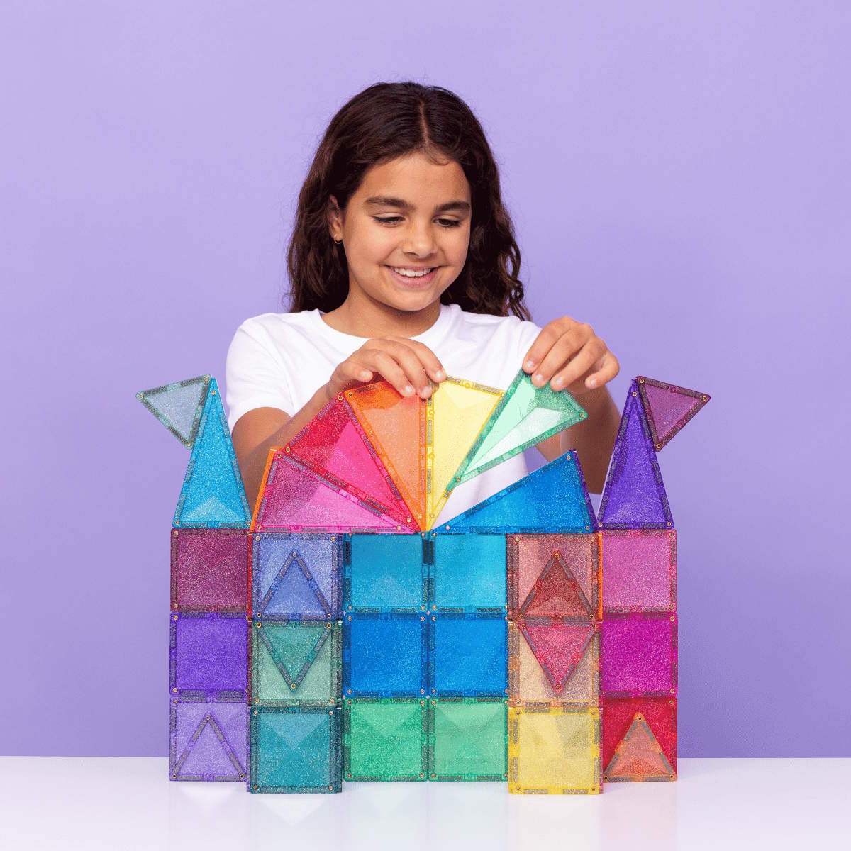 Girl playing with colorful magnetic building tiles against a purple background