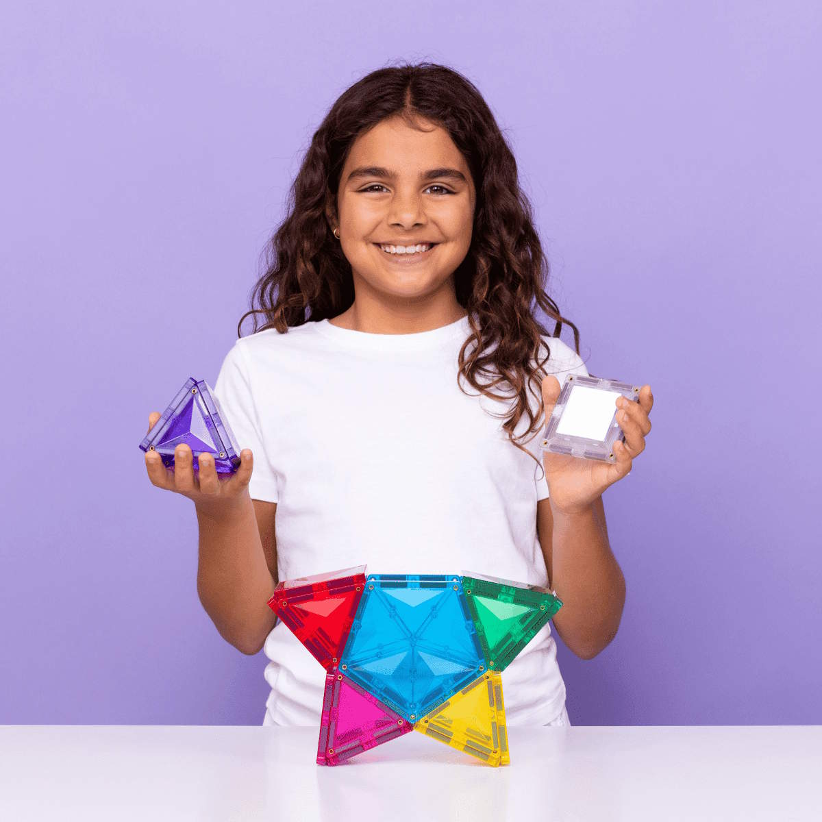 Girl holding colorful Connetix magnetic tiles in a star shape against a purple background